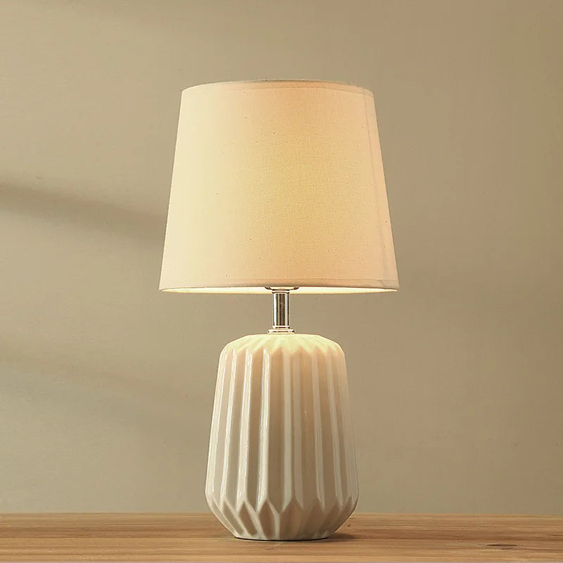 Green cloth shade ceramic lamp glowing softly in bedroom setting