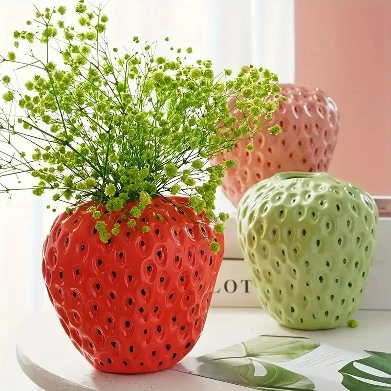 Three strawberry ceramic vases in pink red and cyan shown together