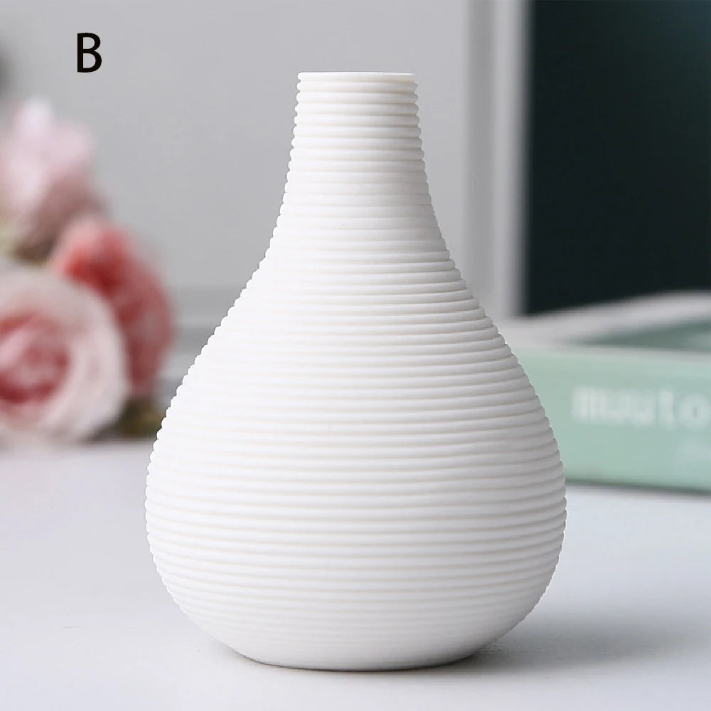 Black ceramic vase D beside large dried alocasia leaf in warm-toned interior setting