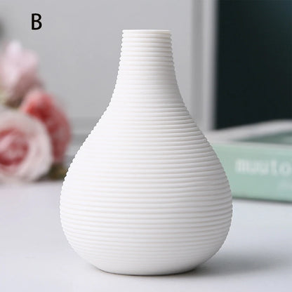 Black ceramic vase D beside large dried alocasia leaf in warm-toned interior setting