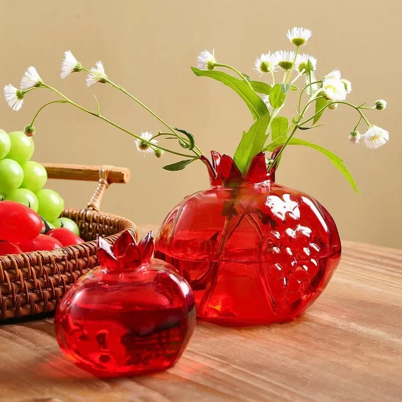 Red glass pomegranate vase holding a single stem on wooden desk