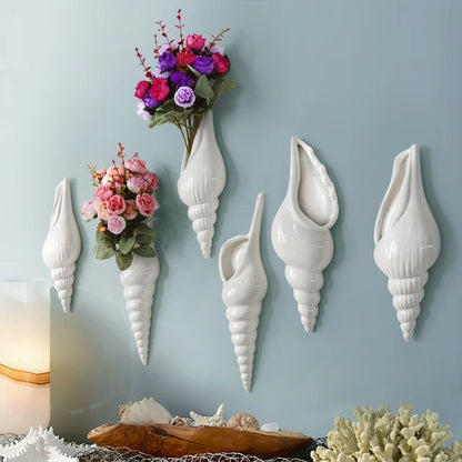 White ceramic conch shell wall vase with dried flower stem on white wall