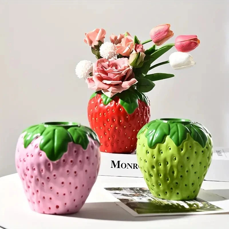 Pink strawberry-shaped ceramic vase holding fresh pink flower stems