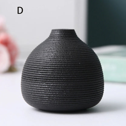 Small cylindrical black ceramic vase C with cotton stem on polished marble surface