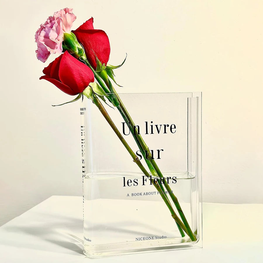 Clear acrylic book-shaped vase with fresh flowers displayed between books on bookshelf