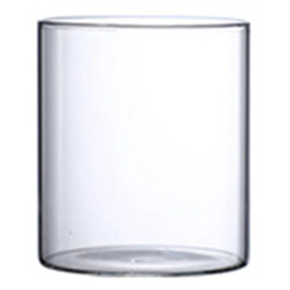 Glass cylinder bud vase with white cotton stem on neutral linen textured surface