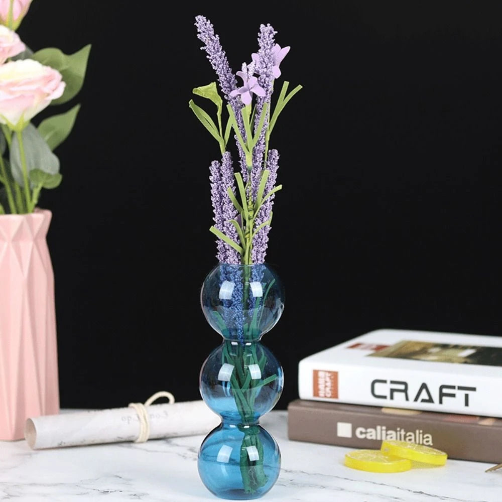 Blue glass hydroponic vase holding trailing ivy stem in water on Scandi shelf